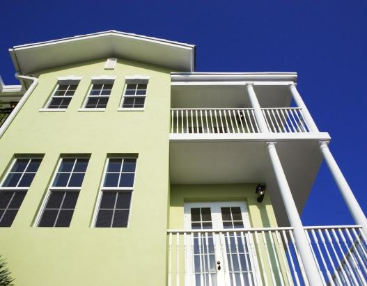 Green building with balconies against blue sky.