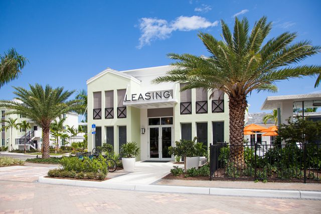 Modern leasing office building with palm trees and clear skies.