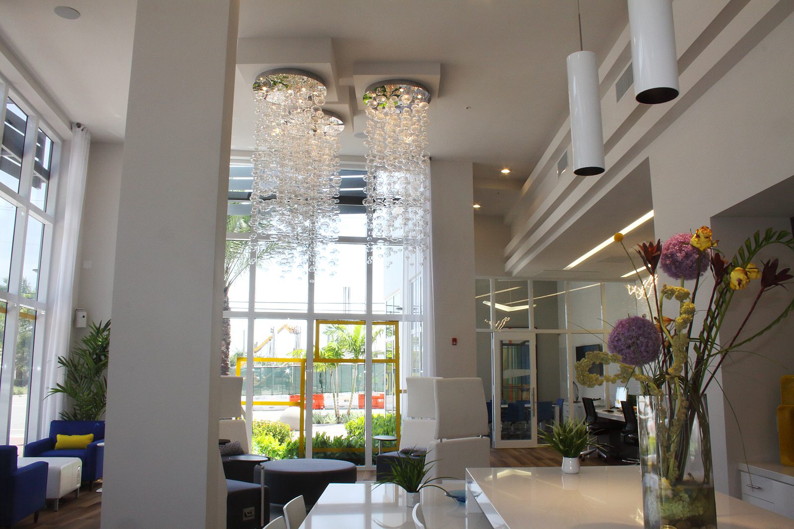 Elegant crystal chandeliers hang in a modern, bright room with large windows.