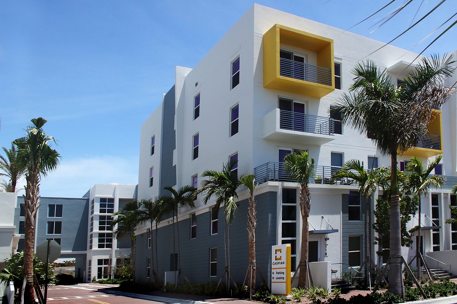 Modern apartment building with palm trees and bright yellow balcony accents.