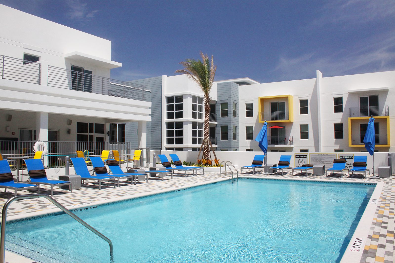 Modern hotel pool area with lounge chairs and palm trees under a clear sky.