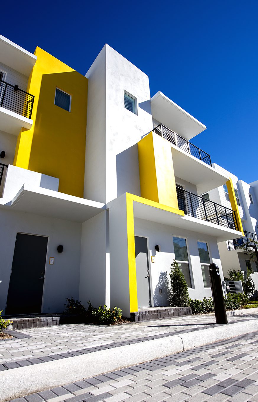 Modern white and yellow apartment building under clear blue sky.