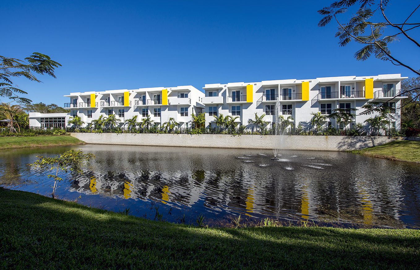 Modern white and yellow building reflecting in a calm water body.