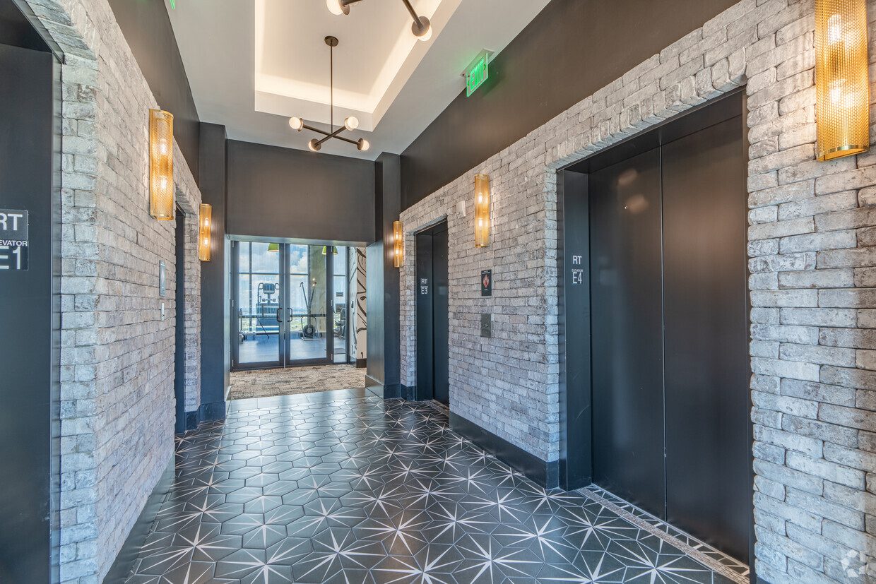 Modern elevator lobby with patterned tile floor and brick walls.