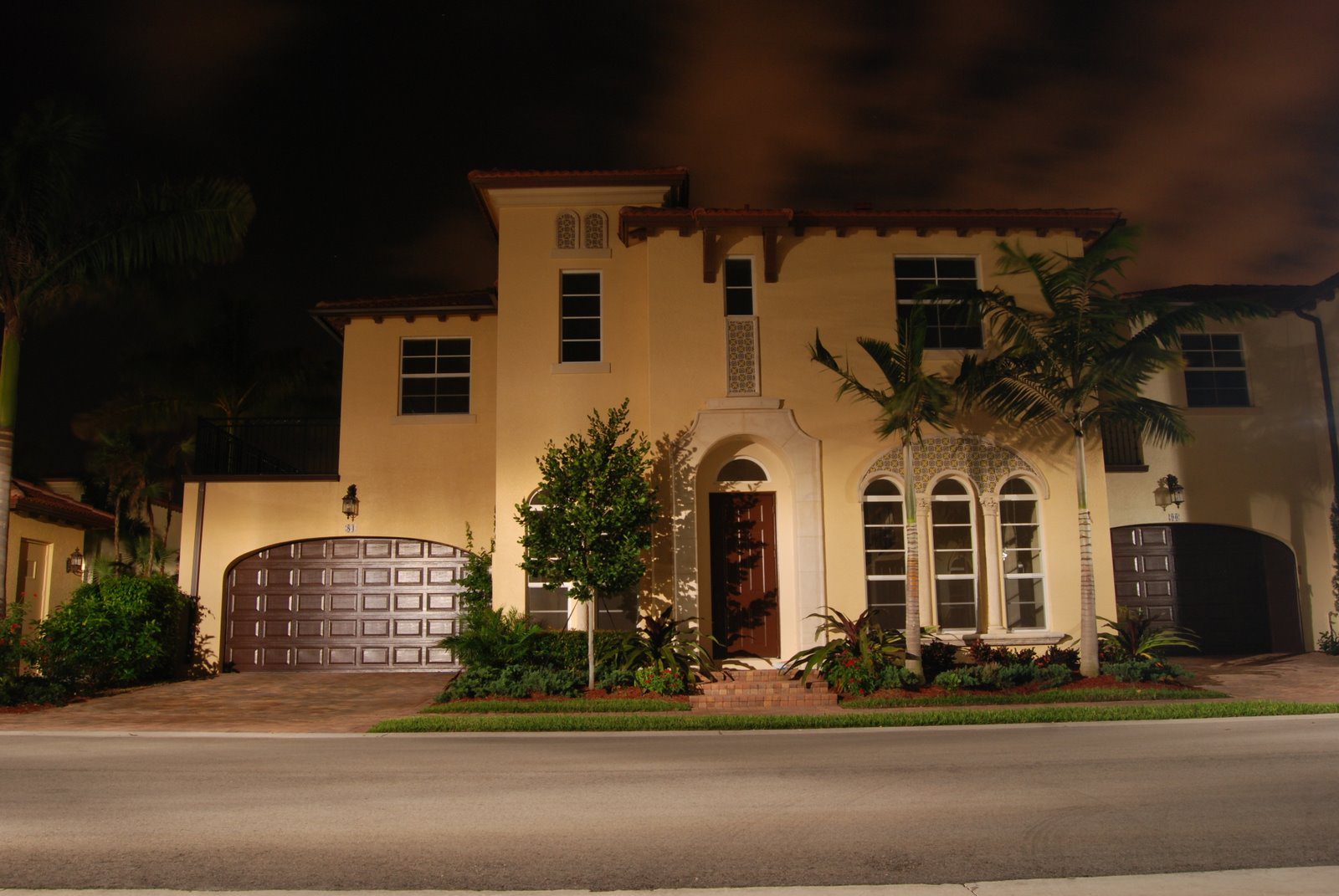 Large house illuminated at night with arched windows and garage.