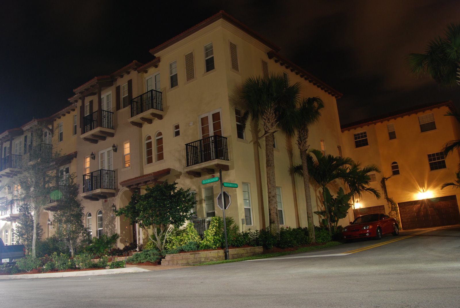 A nighttime street corner with a beige building and palm trees.