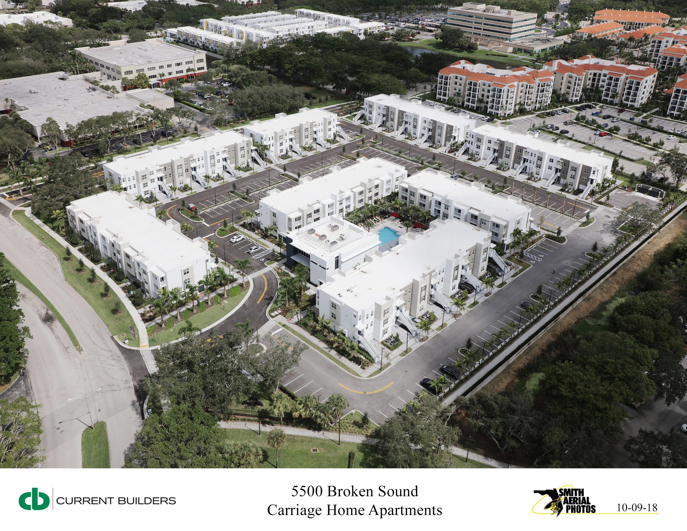 Aerial view of a residential complex with white buildings and a swimming pool.