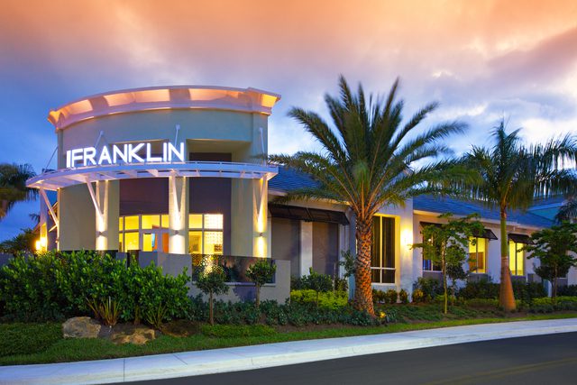 Modern building entrance with palm trees under a colorful sky.