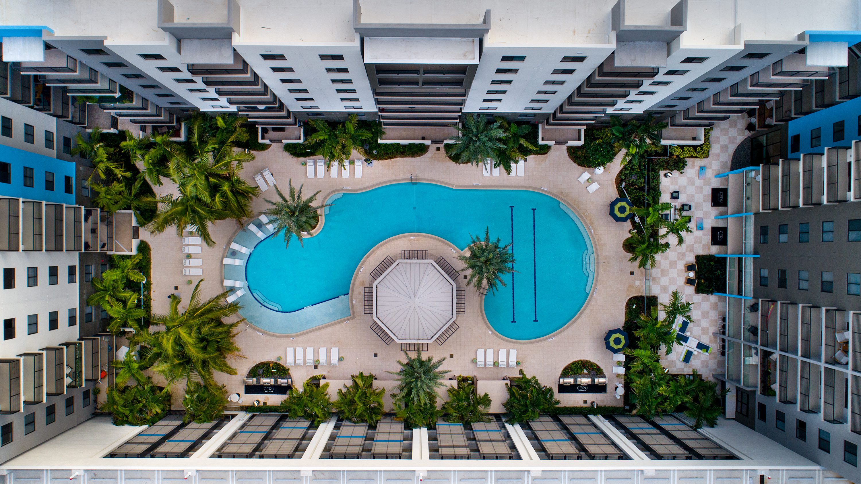 Aerial view of a resort pool with palm trees and surrounding buildings.