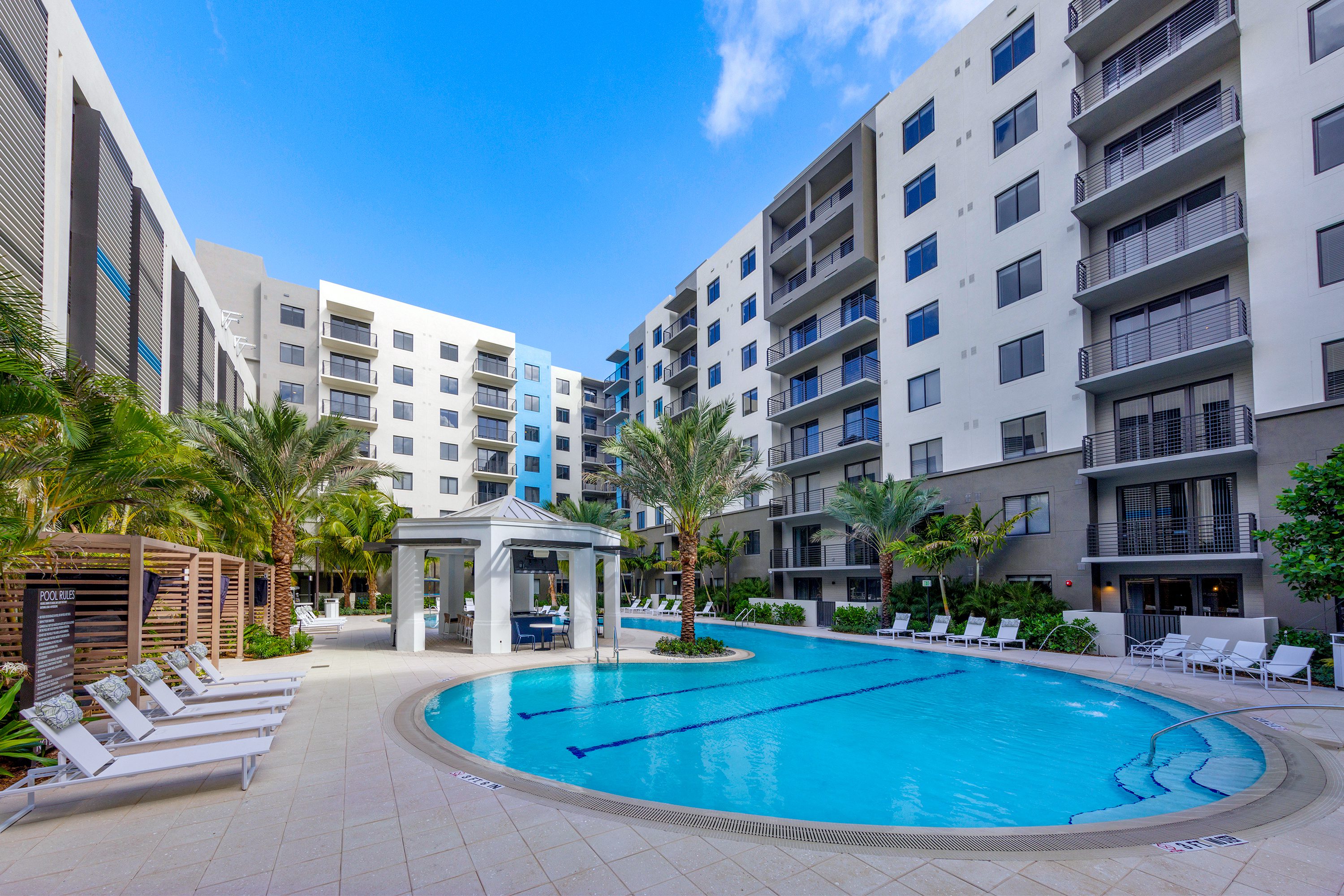 Modern apartment complex with a large outdoor swimming pool and palm trees.