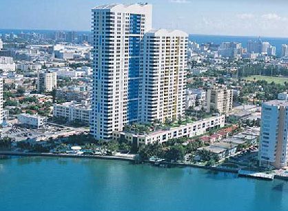 Two tall modern buildings by the waterfront under clear skies.