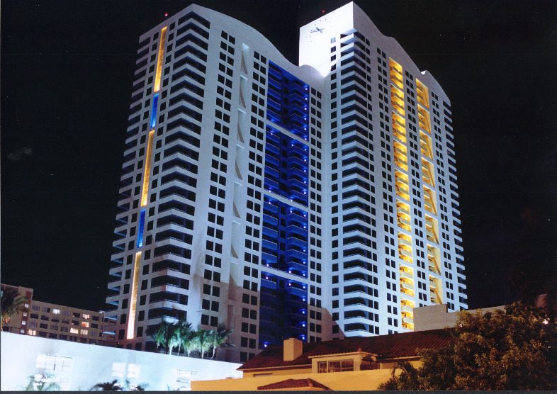 Tall modern building illuminated at night with blue and yellow lights.