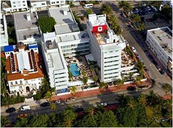 Aerial view of a modern white hotel with a rooftop pool near a busy street.