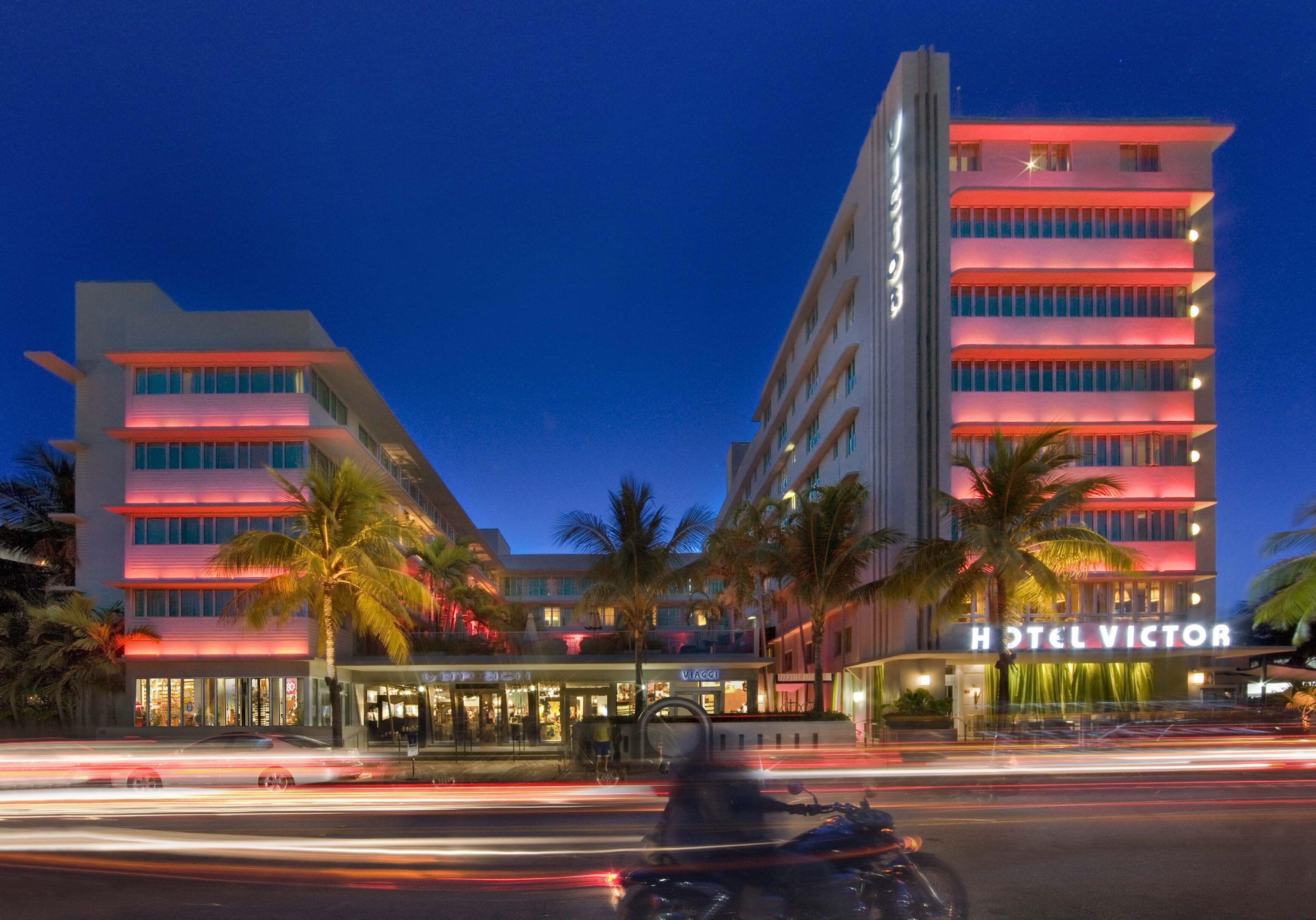 Evening view of a modern hotel with neon lights and palm trees.