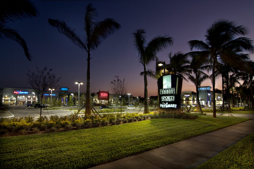 Night view of a palm-lined street near a shopping plaza.