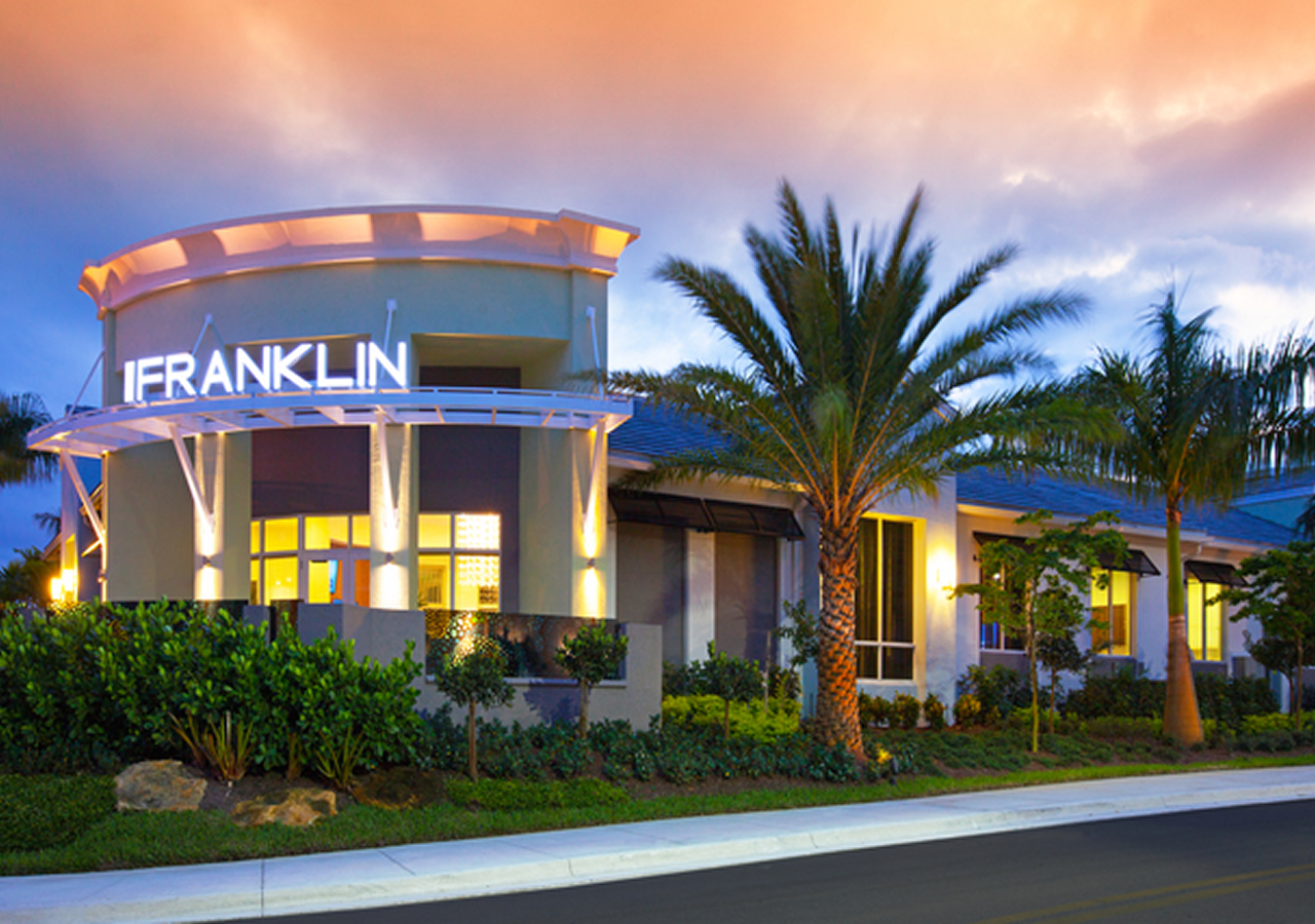 Modern building with palm trees at sunset under a colorful sky.