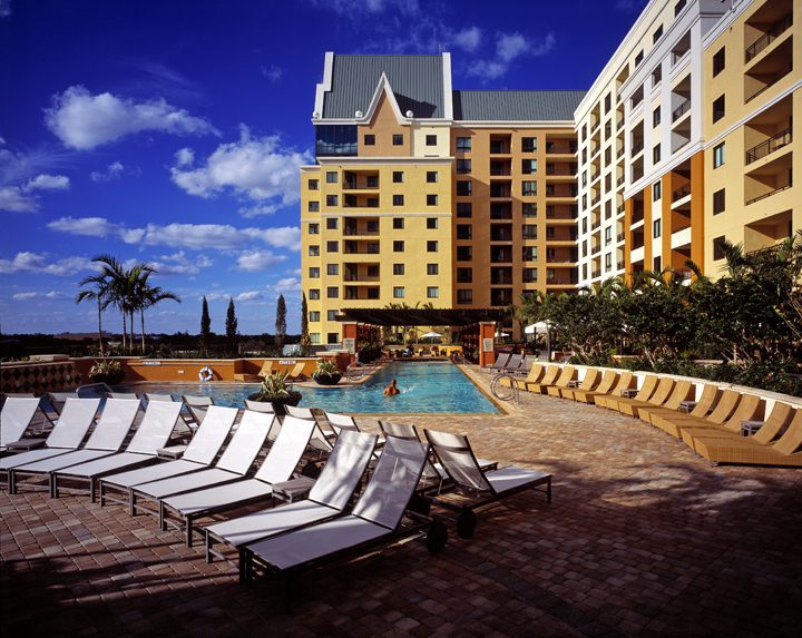Poolside lounge chairs at a sunny resort with a clear blue sky.