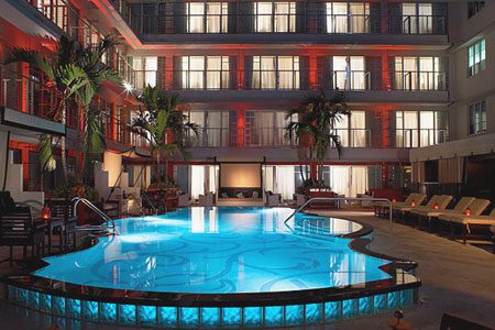 Indoor pool in a stylish hotel atrium with palm trees and warm lighting.