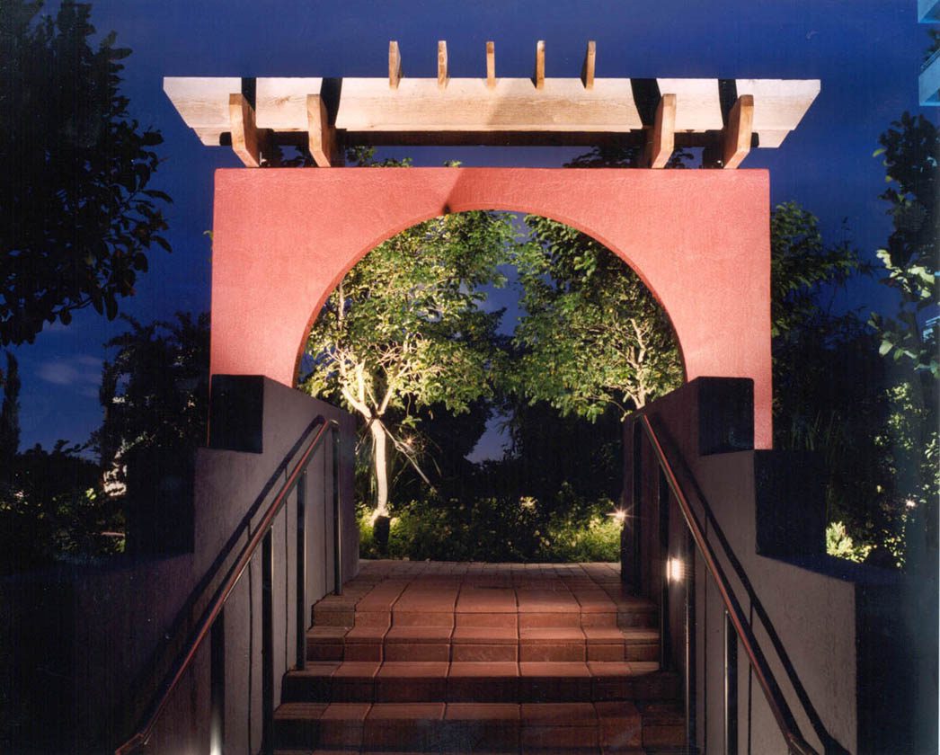 Illuminated archway entrance with steps leading to a garden at night.